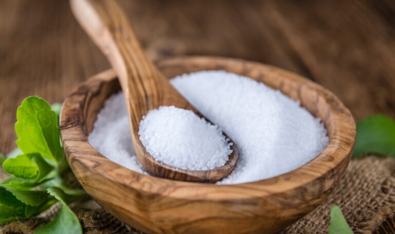 Azúcar light en un bol de madera con una cuchara de madera y rodeado de hojas de stevia.