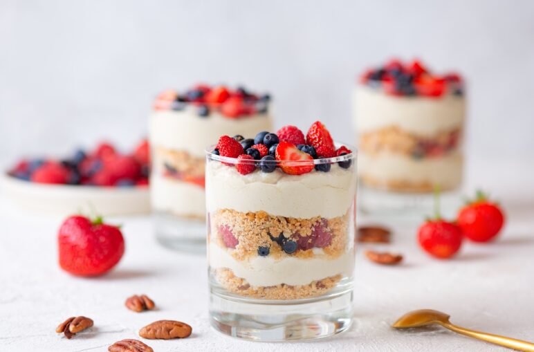 Postre en copas con frutillas, arándanos, crema batida y galleta.