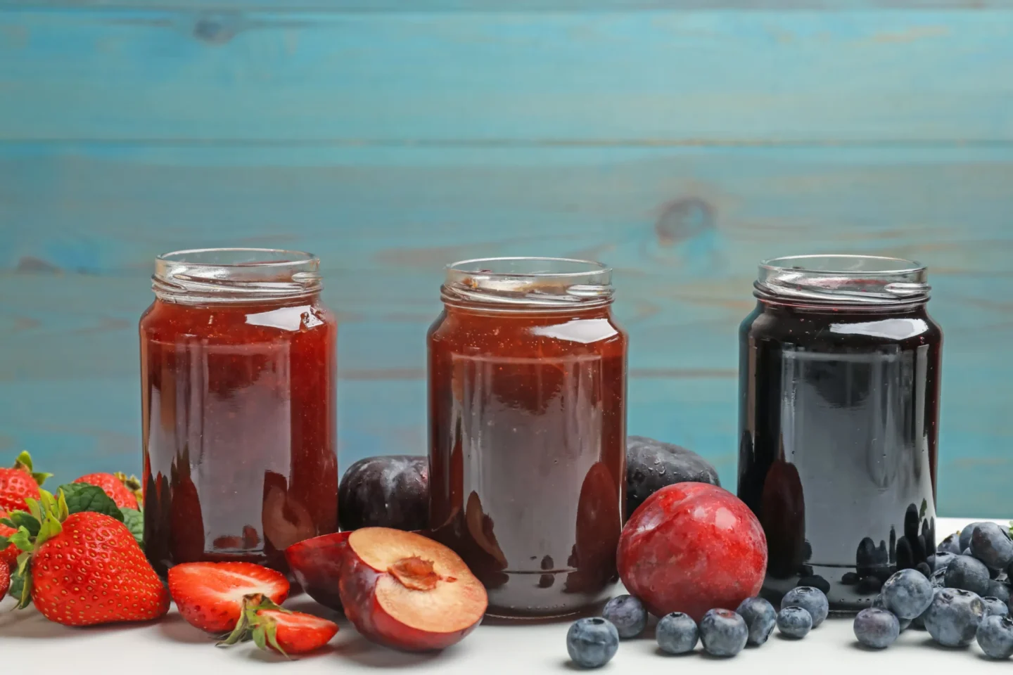 Diferentes mermeladas dulces en tarros e ingredientes sobre mesa blanca
